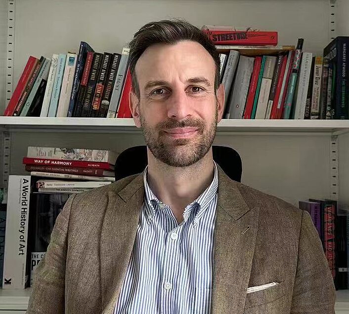 The photo shows professor Ivan Stacy in front of a bookshelf.